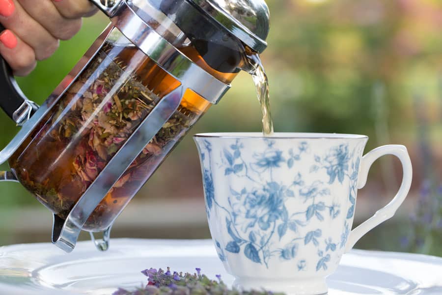 A glass tea pot pouring beautiful tea into a china cup