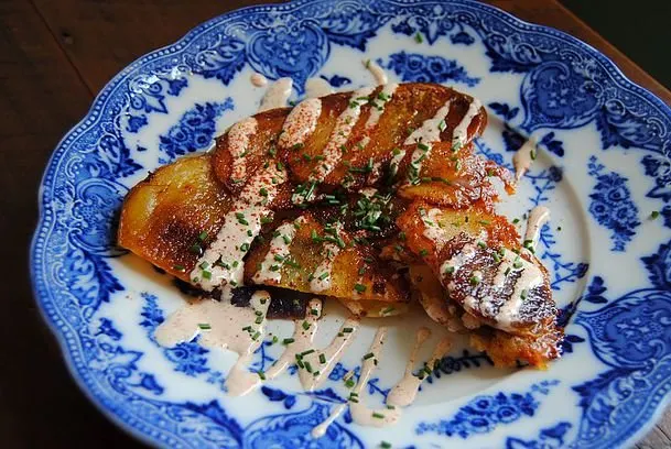 A plated slice of rustic potato cake with chipotle crema on an antique blue plate