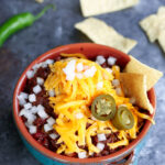 A bowl of bison chili surrounded by chips and chile peppers,