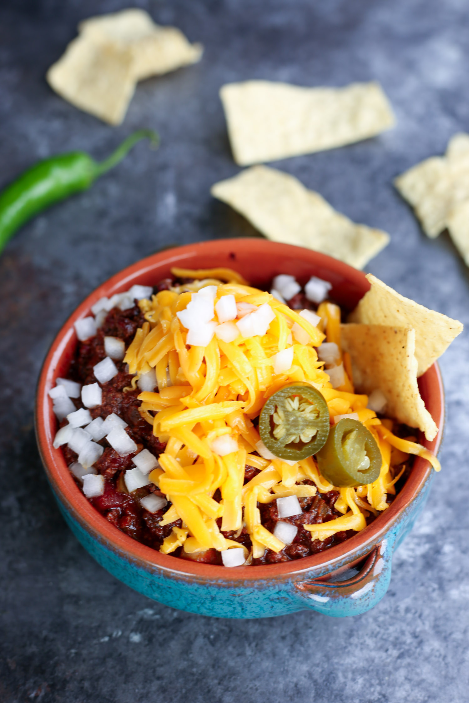 A bowl of bison chili surrounded by chips and chile peppers,