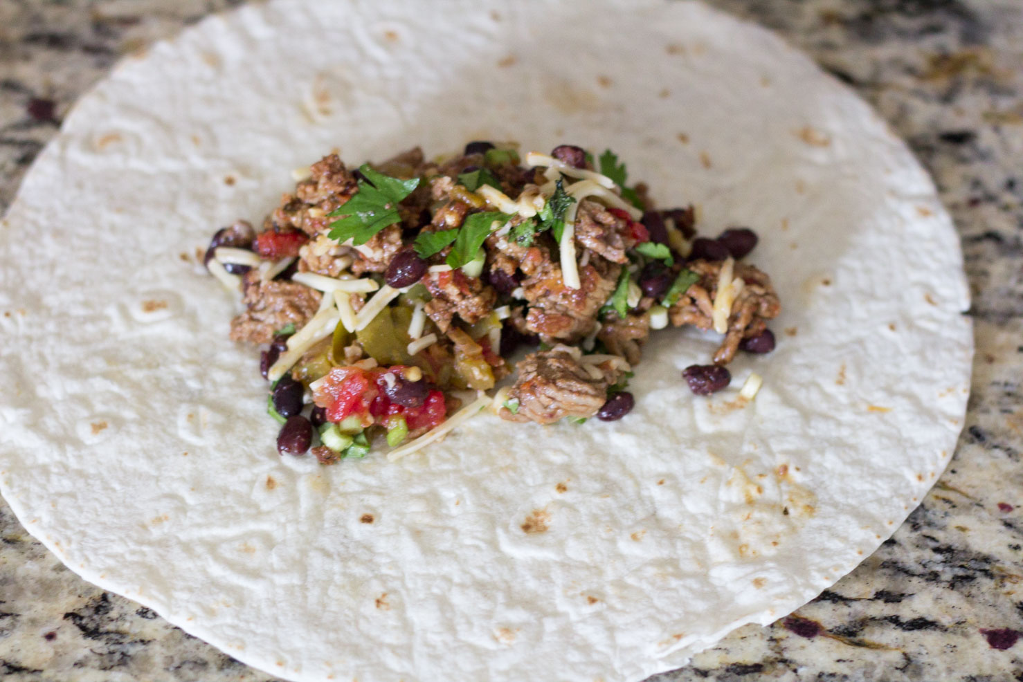 One tortilla with filling prepared to be rolled