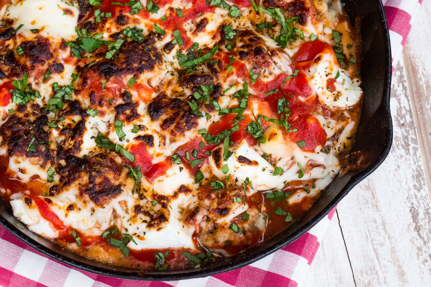 Easy meatballs in a black cast iron skillet with pizza sauce and broiled cheese on top.