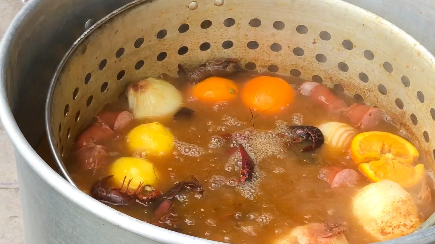 A pot of simmering crawfish boil broth, veggies, sausage, and crawdads. 