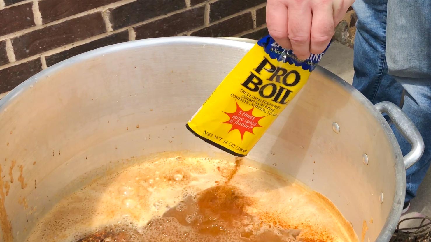 Crawfish boil being made by pouring bags of spices into the stainless steel boiling pot. 