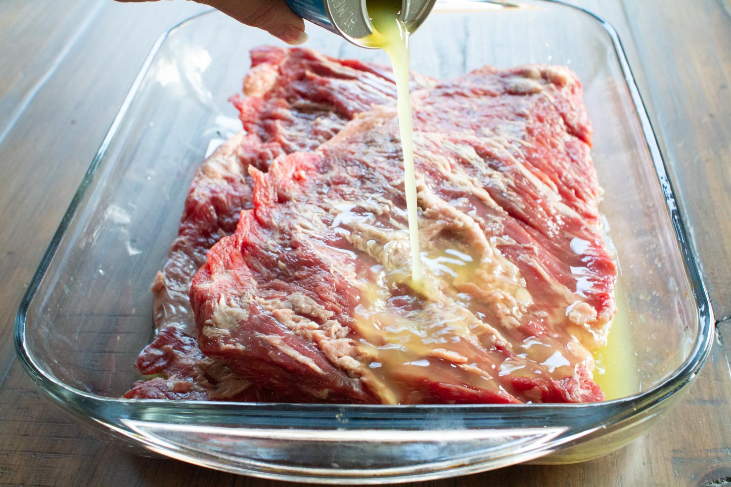 Pineapple juice being poured on skirt steak for the fajita marinade