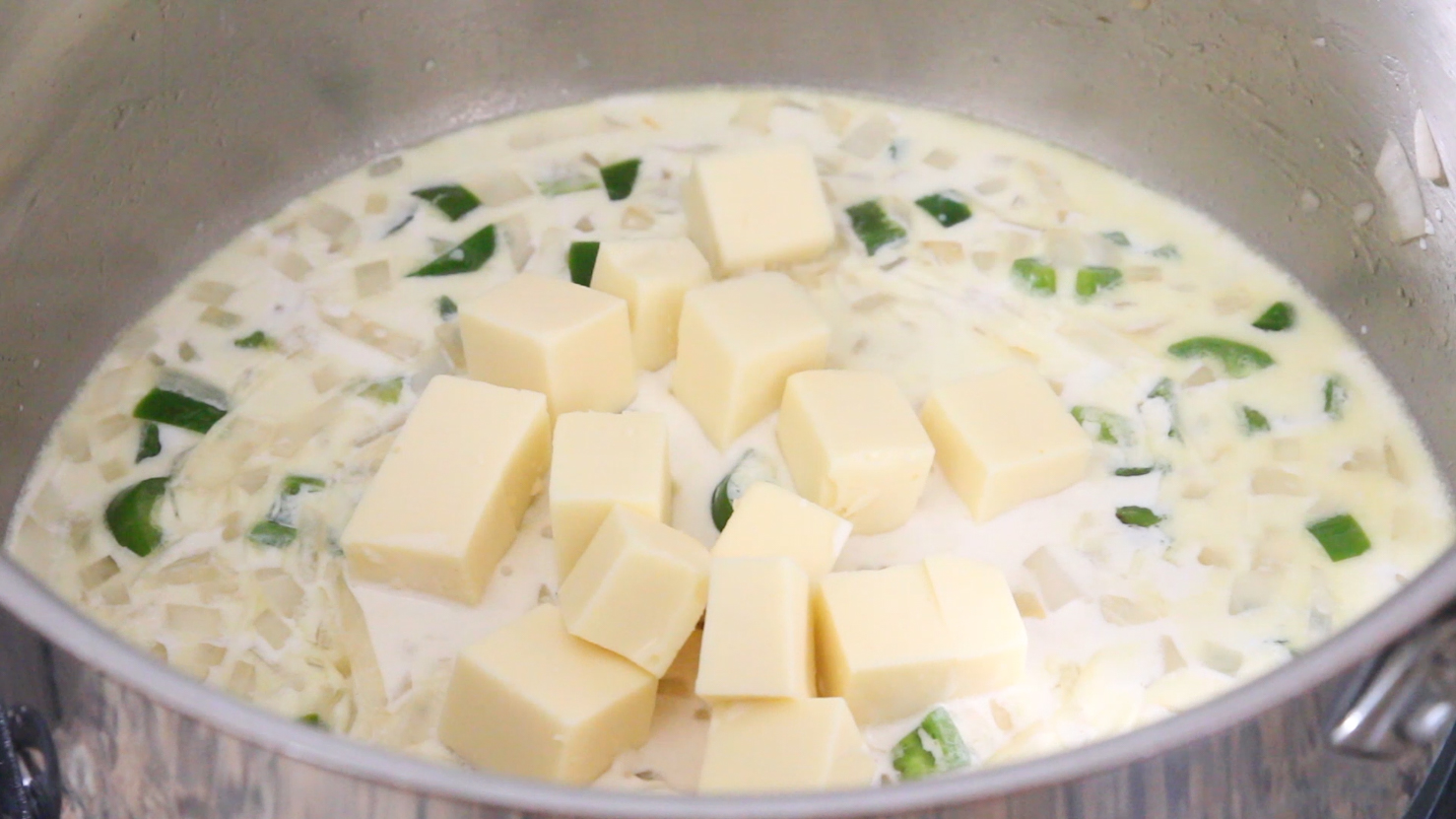 Chunks of queso blanco being added to the queso