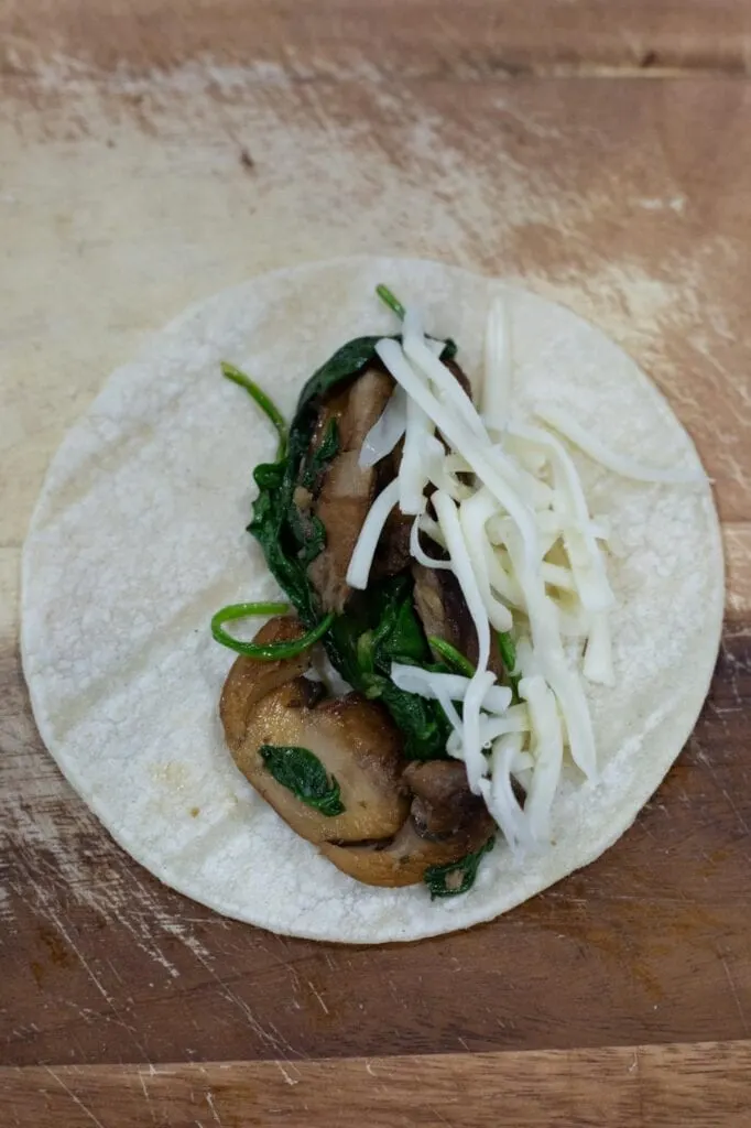 A corn tortilla with mushroom and spinach filling for making enchiladas
