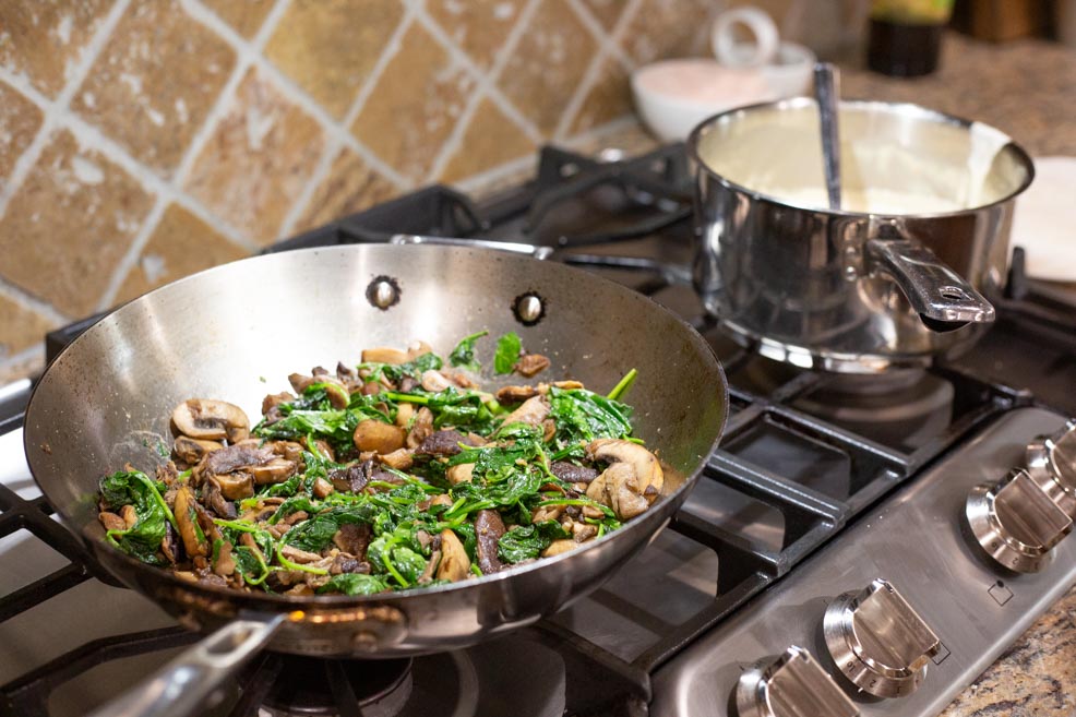 A stove top filled with ingredients for making spinach and mushroom enchiladas