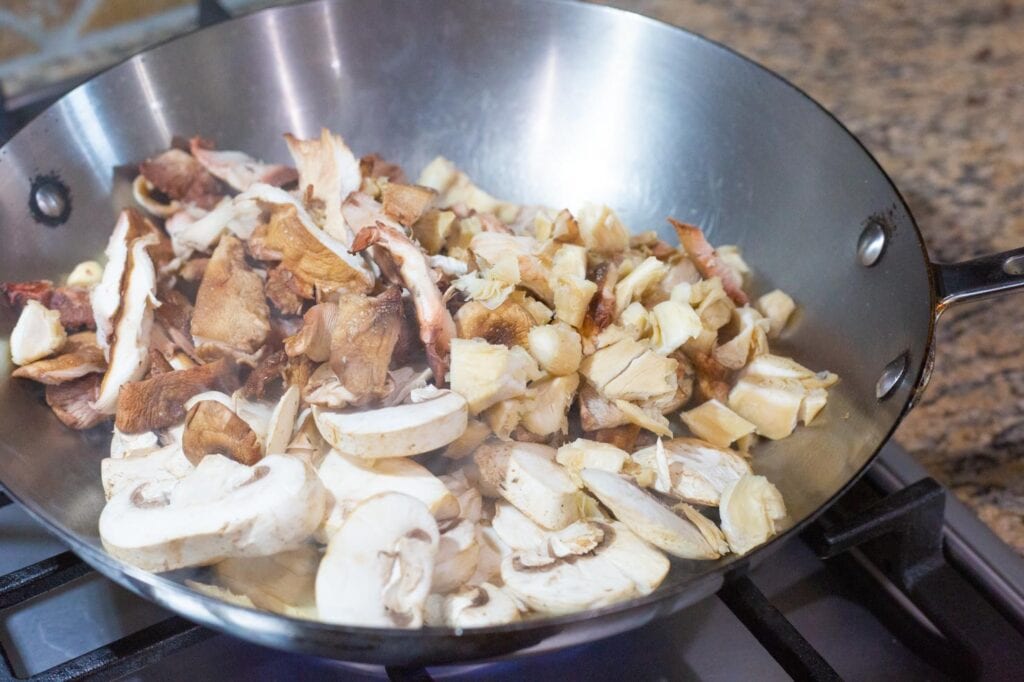 A pan cooking sliced shiitake and oyster mushrooms for enchiladas