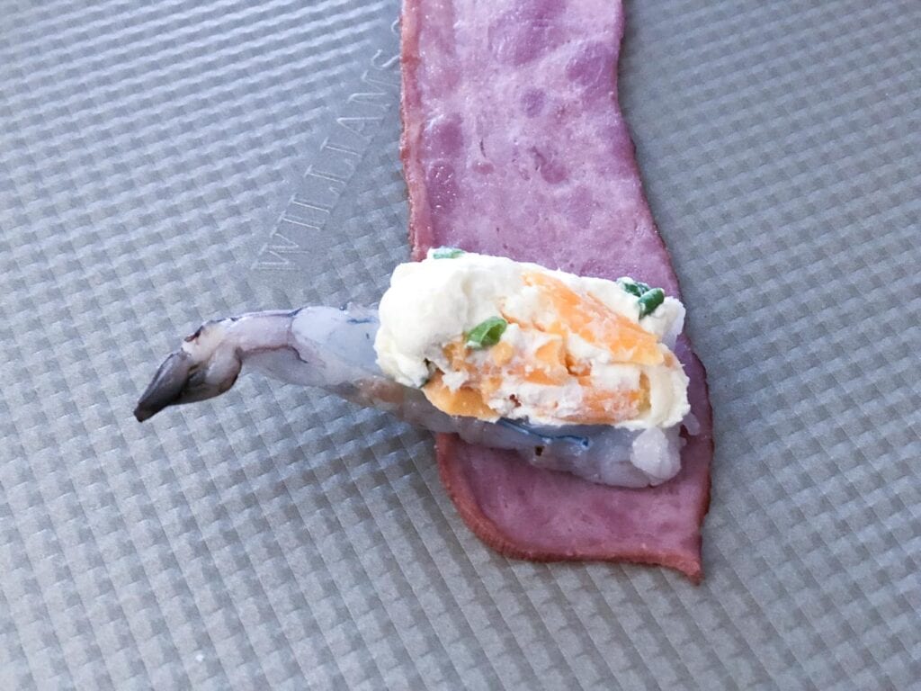 A cheese stuffed shrimp laying on a fresh piece of bacon
