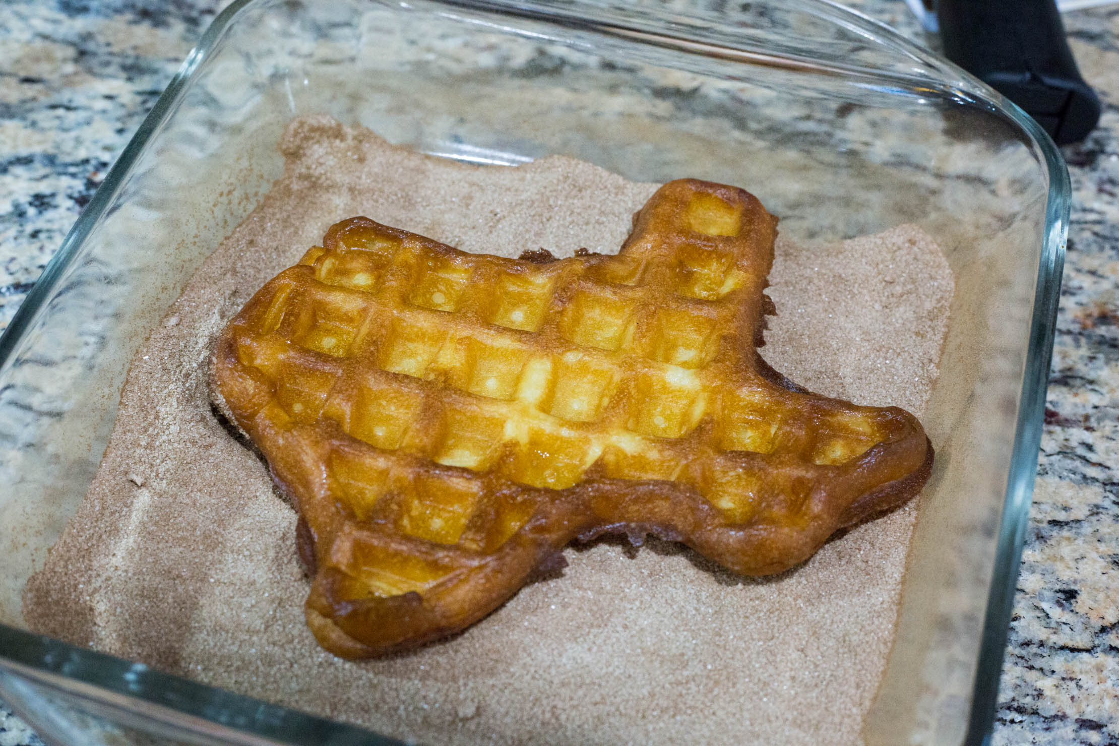 A churro waffle being coated in cinnamon sugar