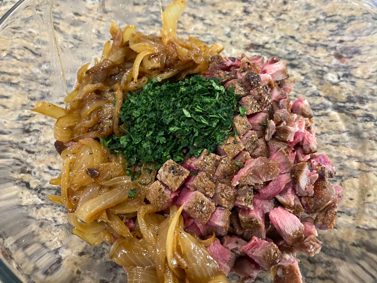 A bowl of seared filet mignon cubes, caramelized onion, and herbs 