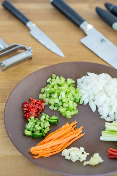 A colorful plate of vegetables chopped into diffferent knife cuts, and the knives used. 