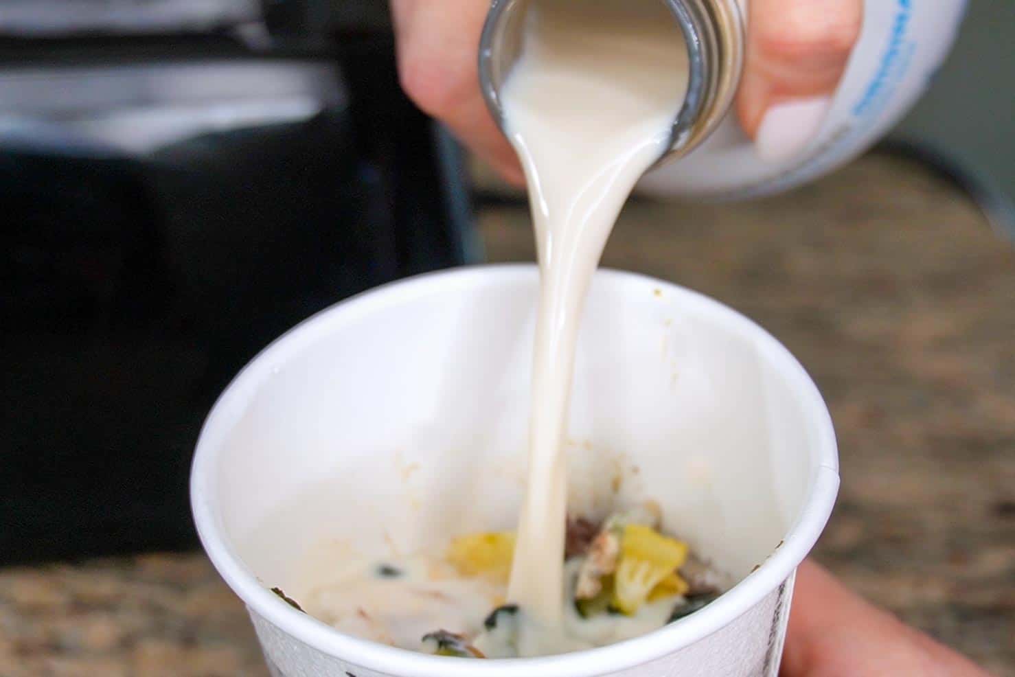 Milk being poured into the cup of frozen ingredients 