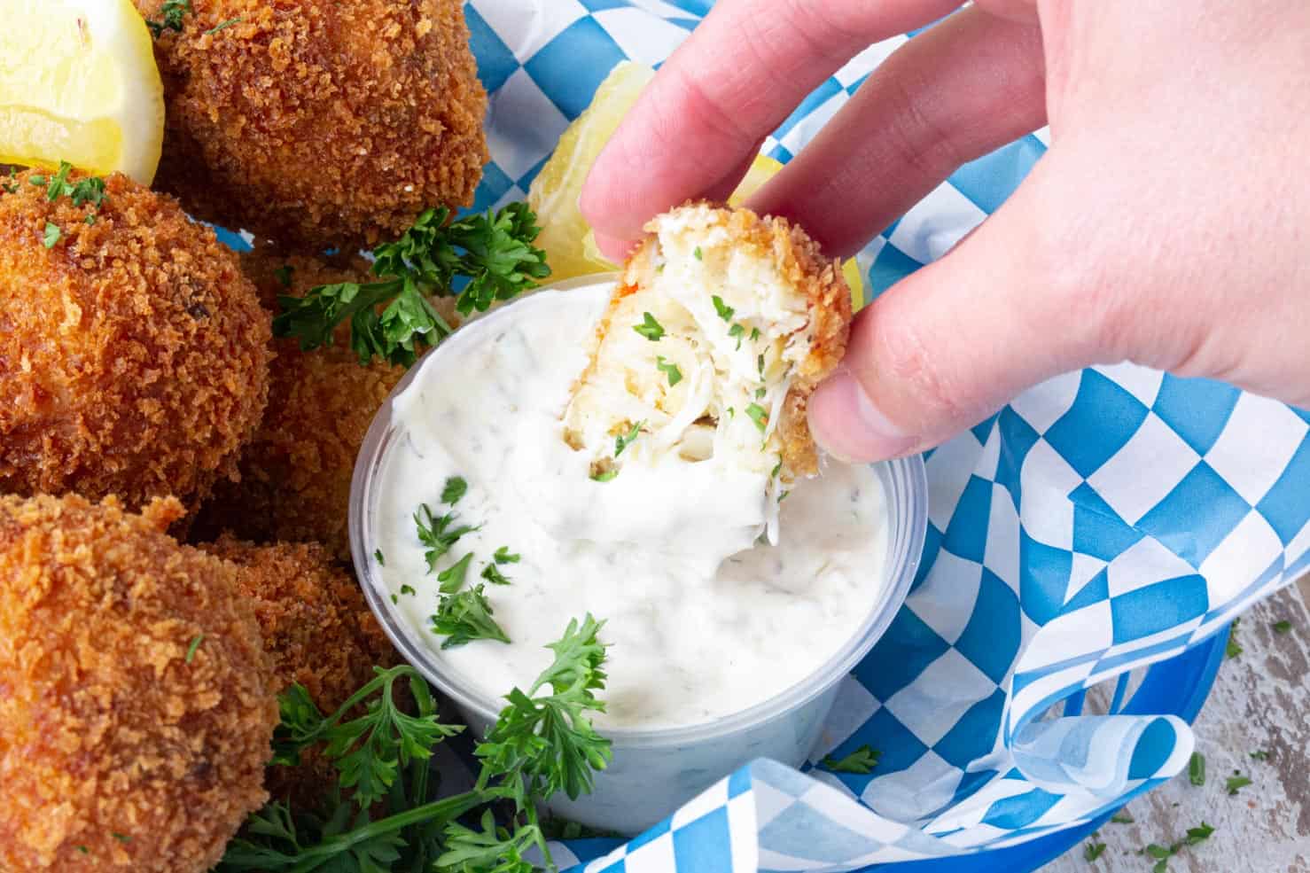 A crab ball being dunked in tartar sauce. 