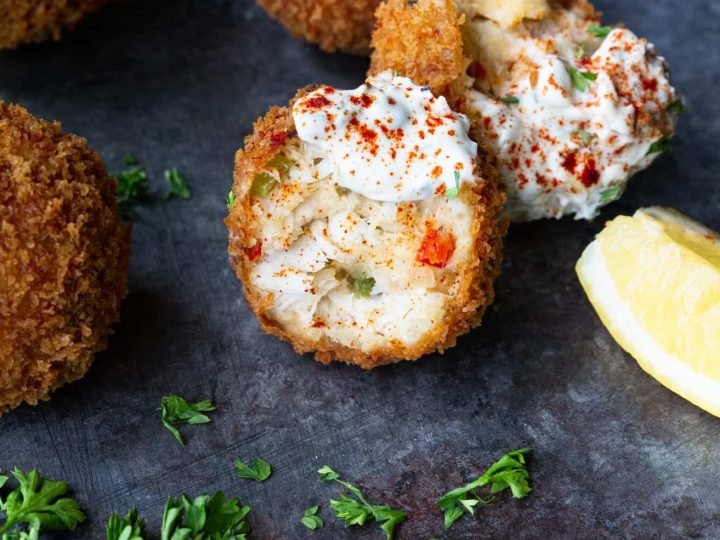 A crab ball sliced in half on a black background with parsley and lemon