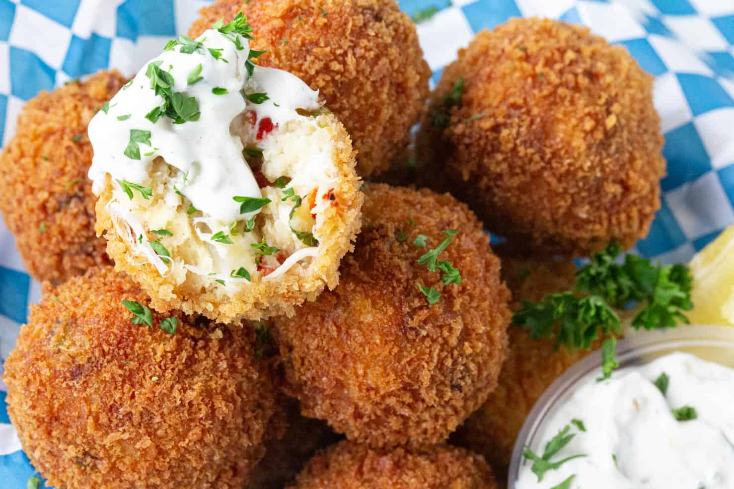 A basket of delicious golden brown fried crab balls being dunked in tartar sauce and spritzed with lemon. 