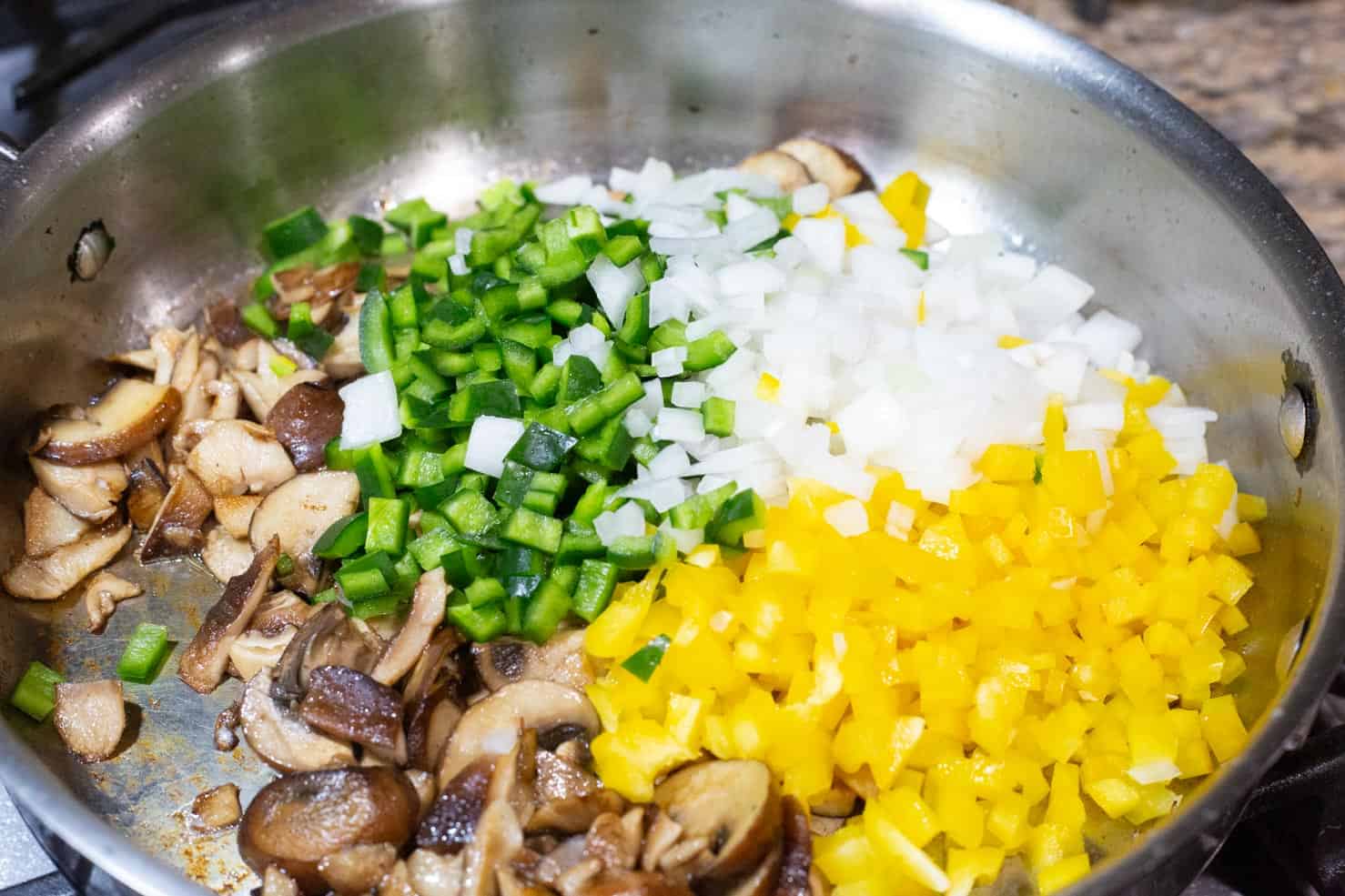 A saute pan full of poblano peppers, onion, and seared mushrooms, on a stove. 