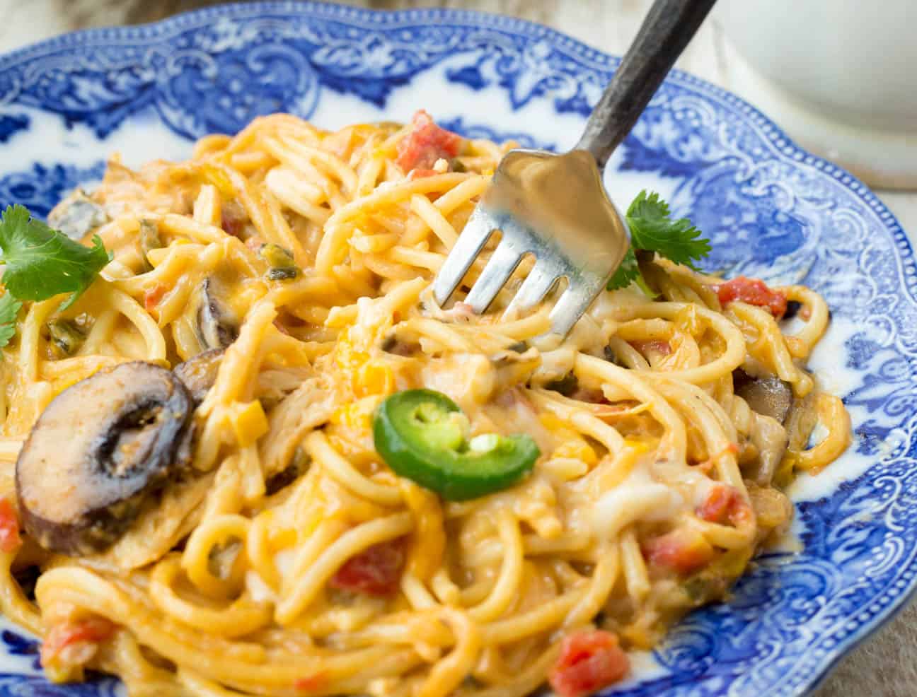 A close up of a fork scooping out a bite of cheesy chicken spaghetti made with Rotel and Velveeta cheese sauce. 