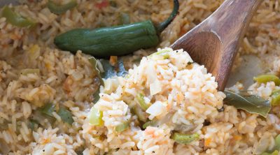 A wooden spoonful full of fluffy mexican rice with peppers.