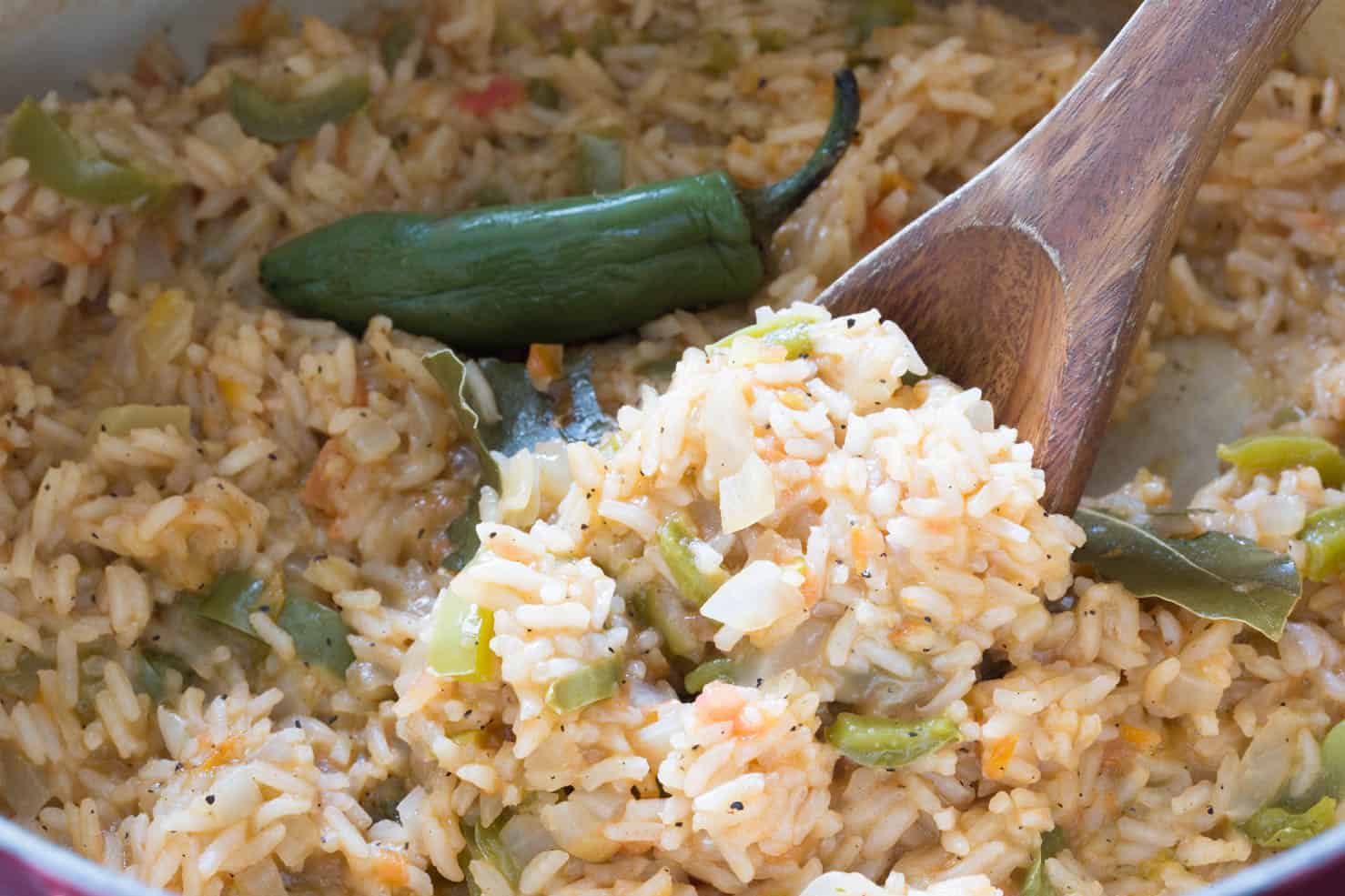 A pan full of fluffy mexican rice with tomatoes, peppers, and onions, being held up by a spoon. 