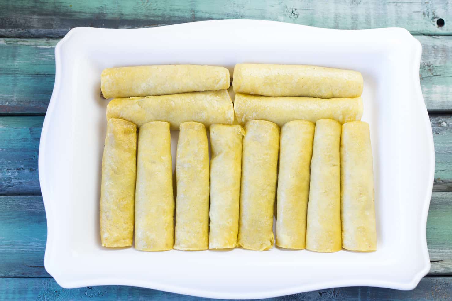 A white casserole dish of rolled cheese enchiladas awaiting sauce. 