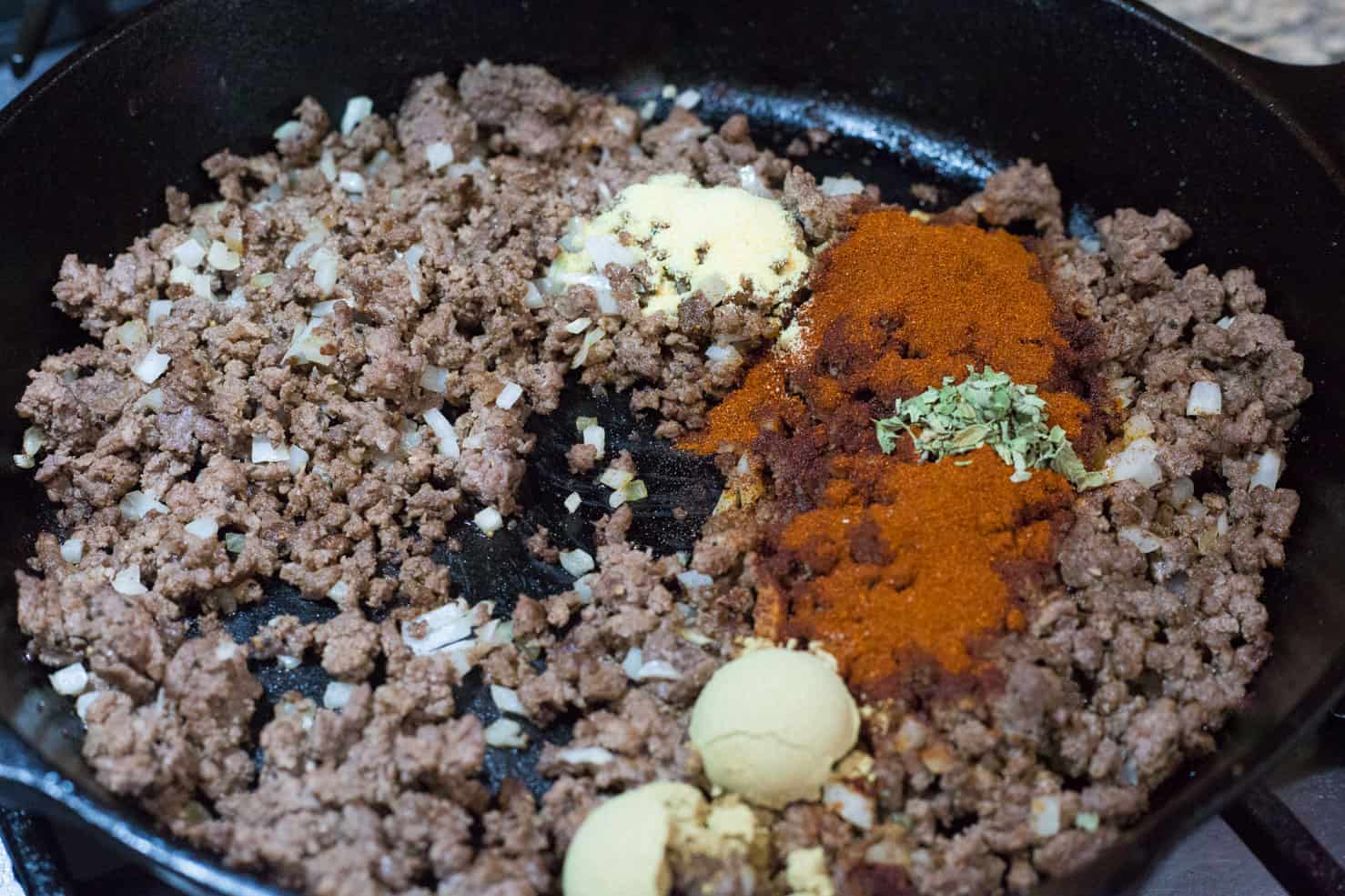 A cast iron skillet filled with cooked beef, onion, and the spices for the recipe.