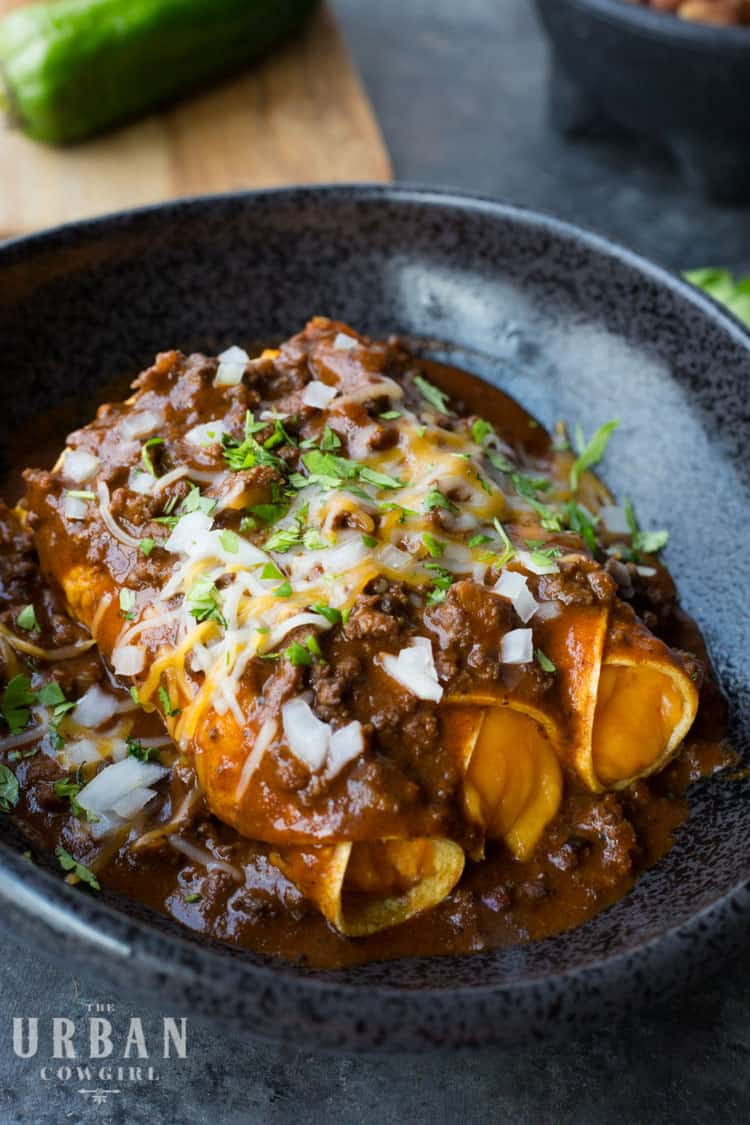 A close up of cheese Enchiladas on a black plate topped with white onion and herbs.