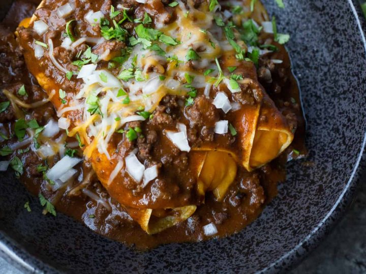 Cheese enchiladas on a black plate topped with chili gravy