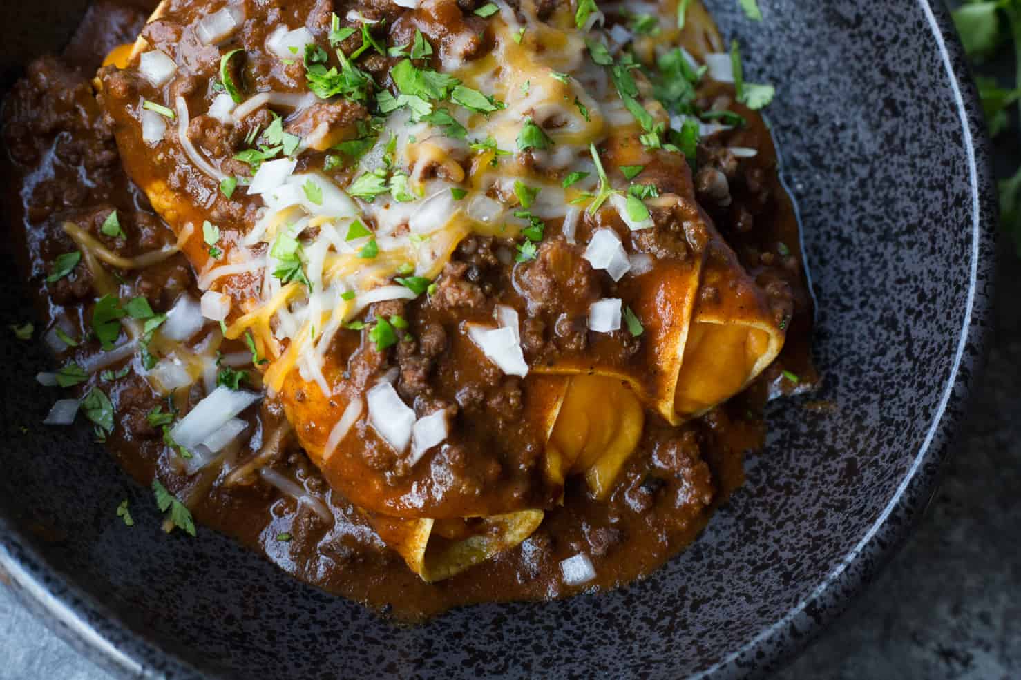 Cheese enchiladas on a black plate topped with chili gravy