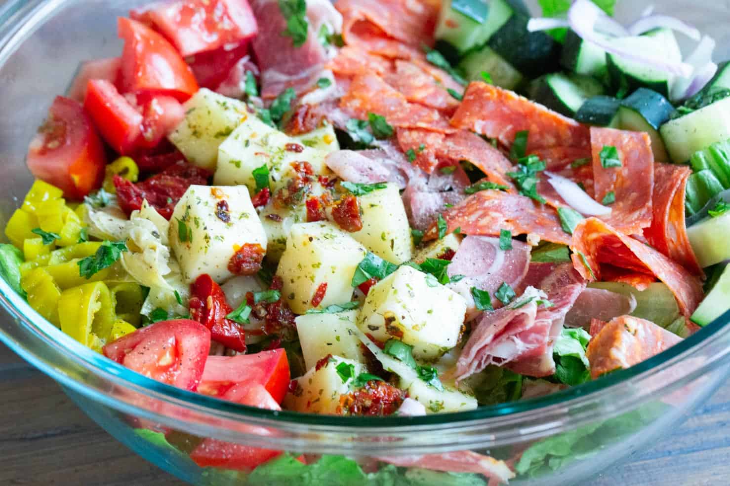 A bright bowl of marinated cheese, candied tomatoes, cured meats, and bright peppers in a sunny window. 