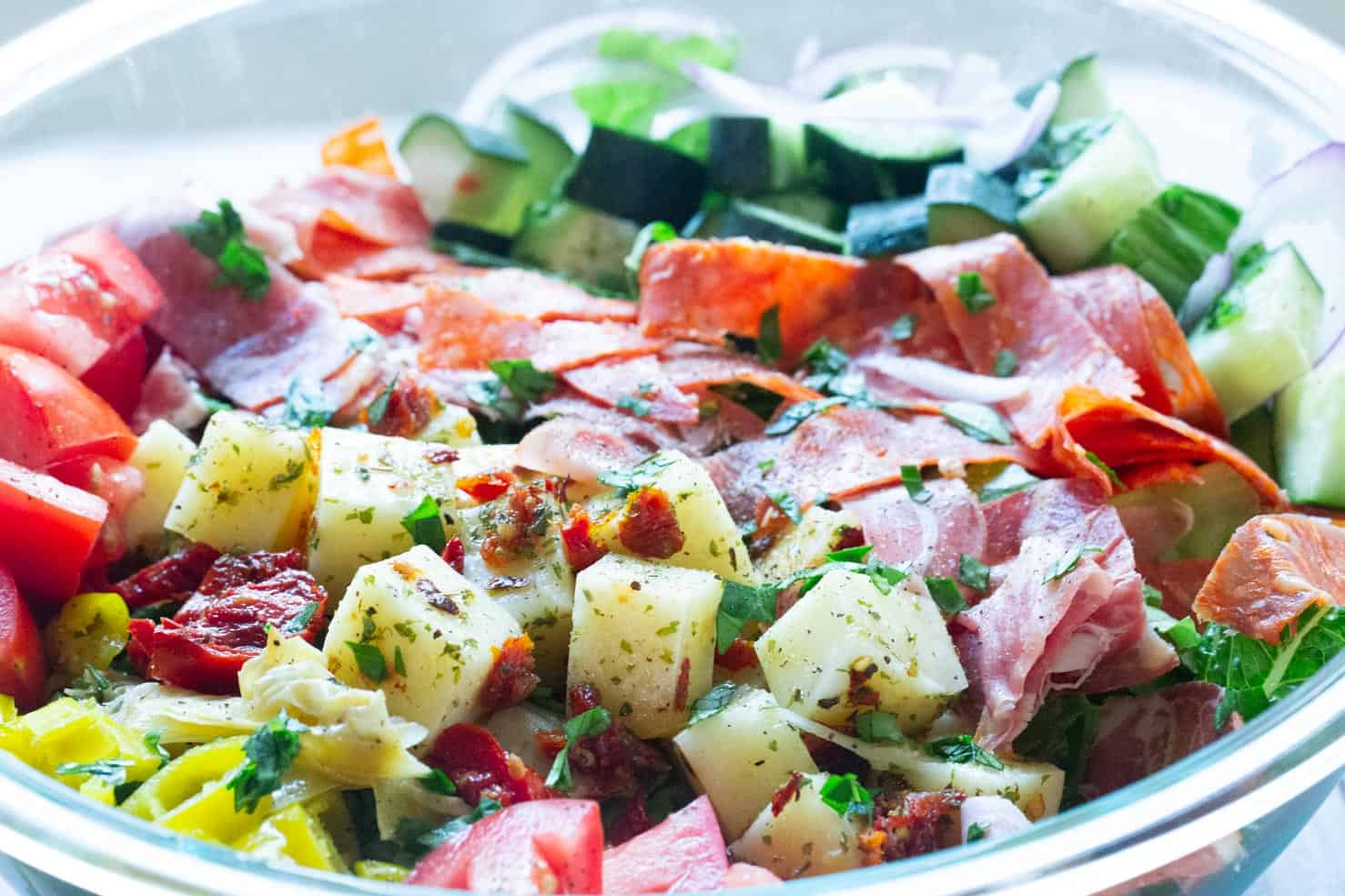 A bright bowl of marinated cheese, candied tomatoes, cured meats, and bright peppers.