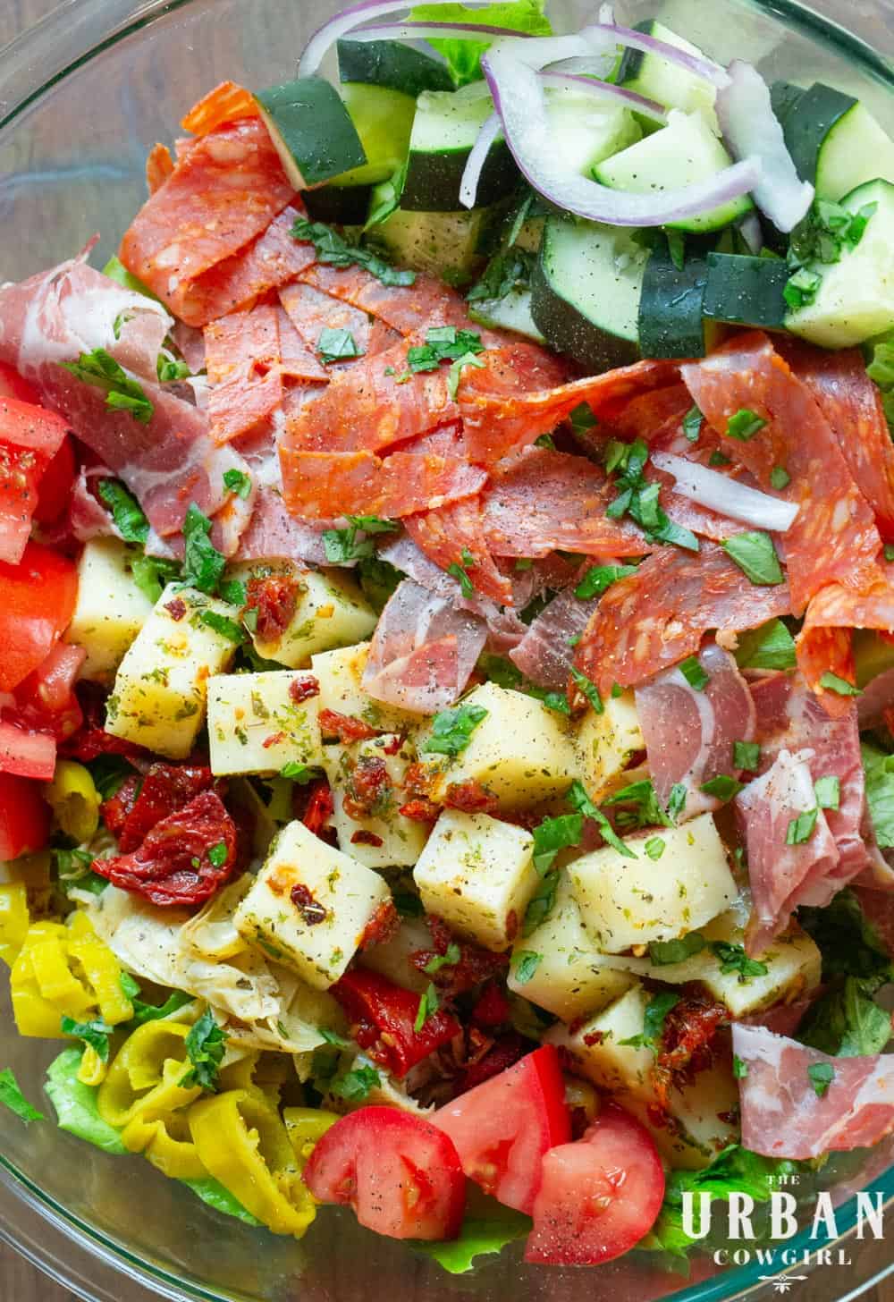 A bright bowl of antipasto salad, marinated cheese, candied tomatoes, cured meats, and bright peppers.