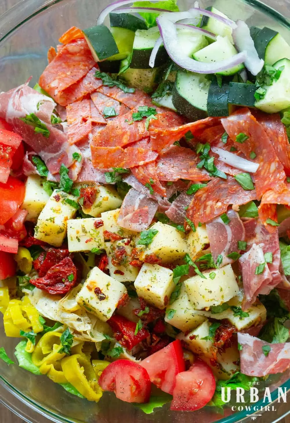 A bright bowl of antipasto salad, marinated cheese, candied tomatoes, cured meats, and bright peppers.