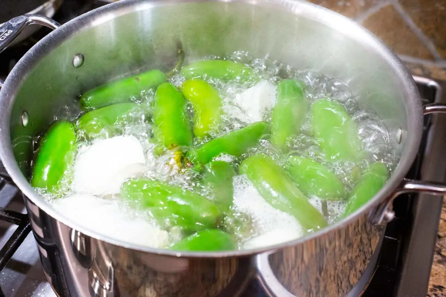jalapenos and onion in the water bath being boiled on a stove