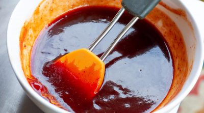 A beautiful bowl of red, strawberry barbecue sauce with a brush.