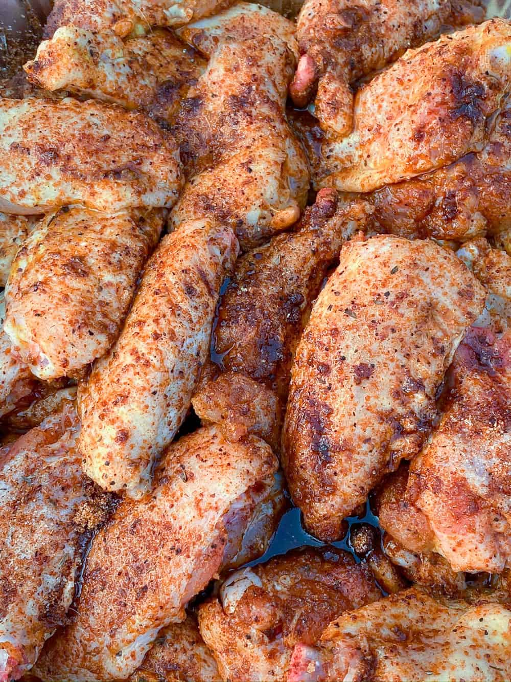 A disposable pan full of chicken wings tossed in a generous amount of barbecue rub. 