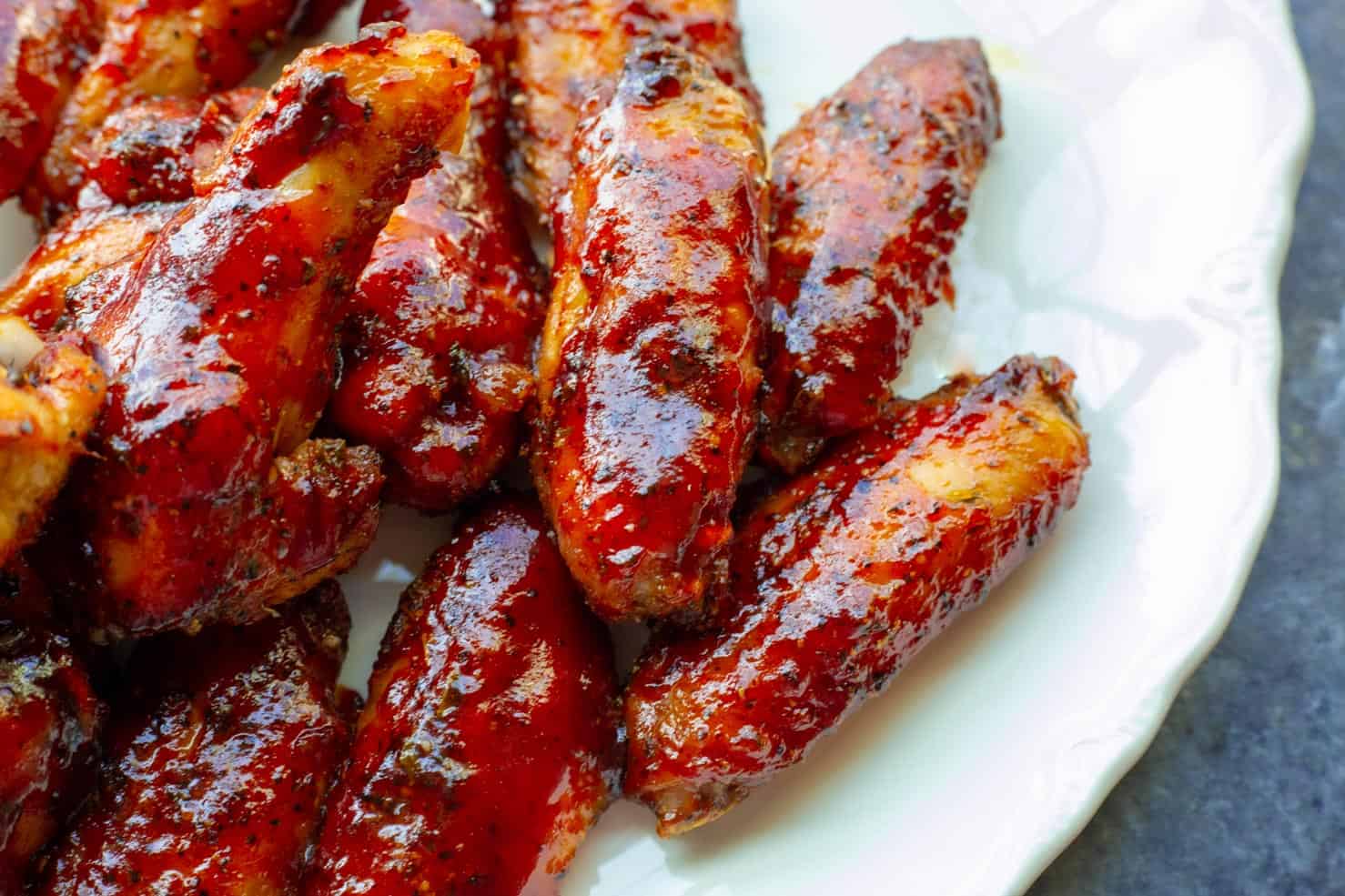 A plate containing smoked chicken wings with a shiny strawberry barbecue sauce. 