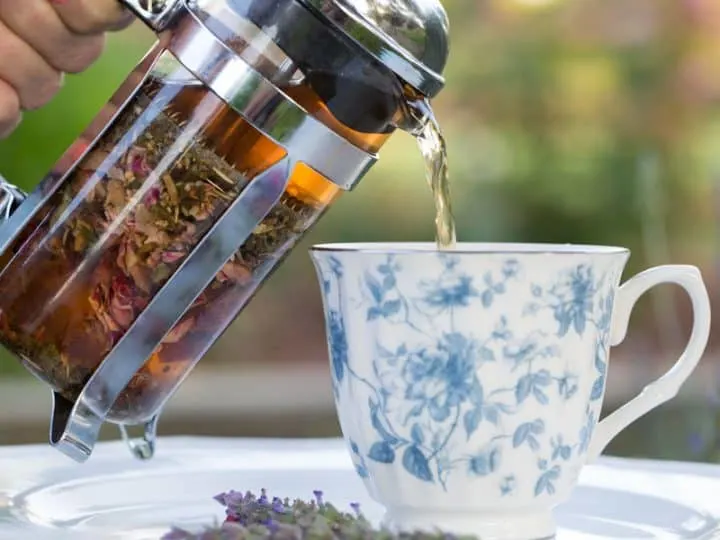 A beautiful floral tea cup being poured into from a french press filled with tea.