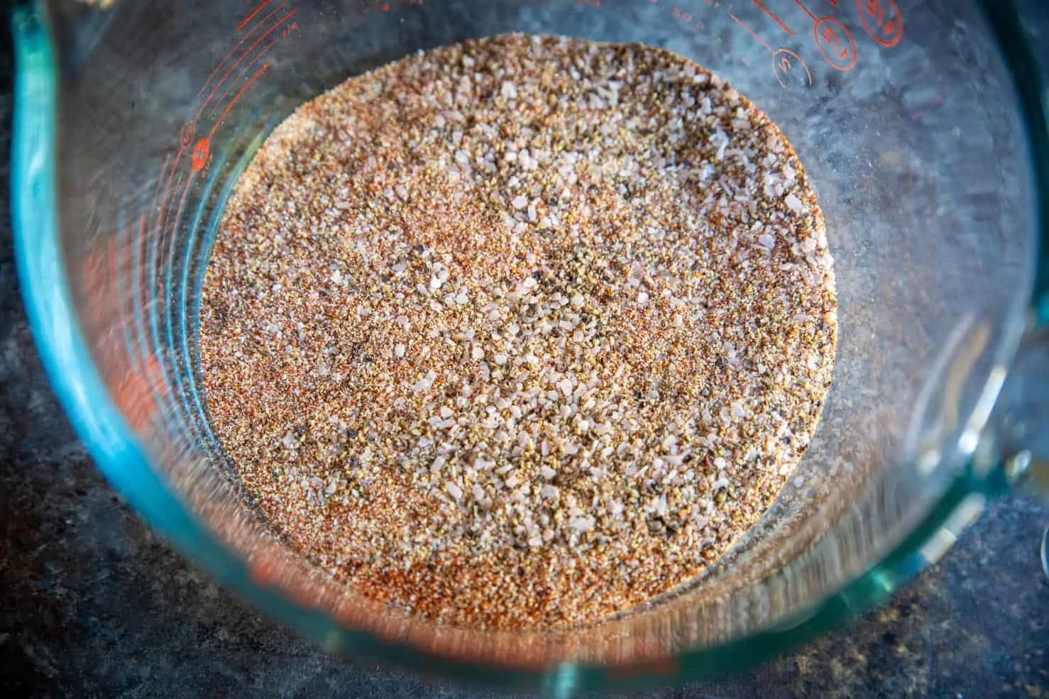 A glass measuring cup full of mixed spices which create the carne asada rub.