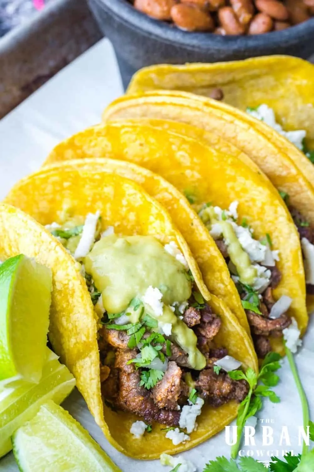 A pan of steak street tacos covered in a creamy jalapeno sauce with cheese and limes