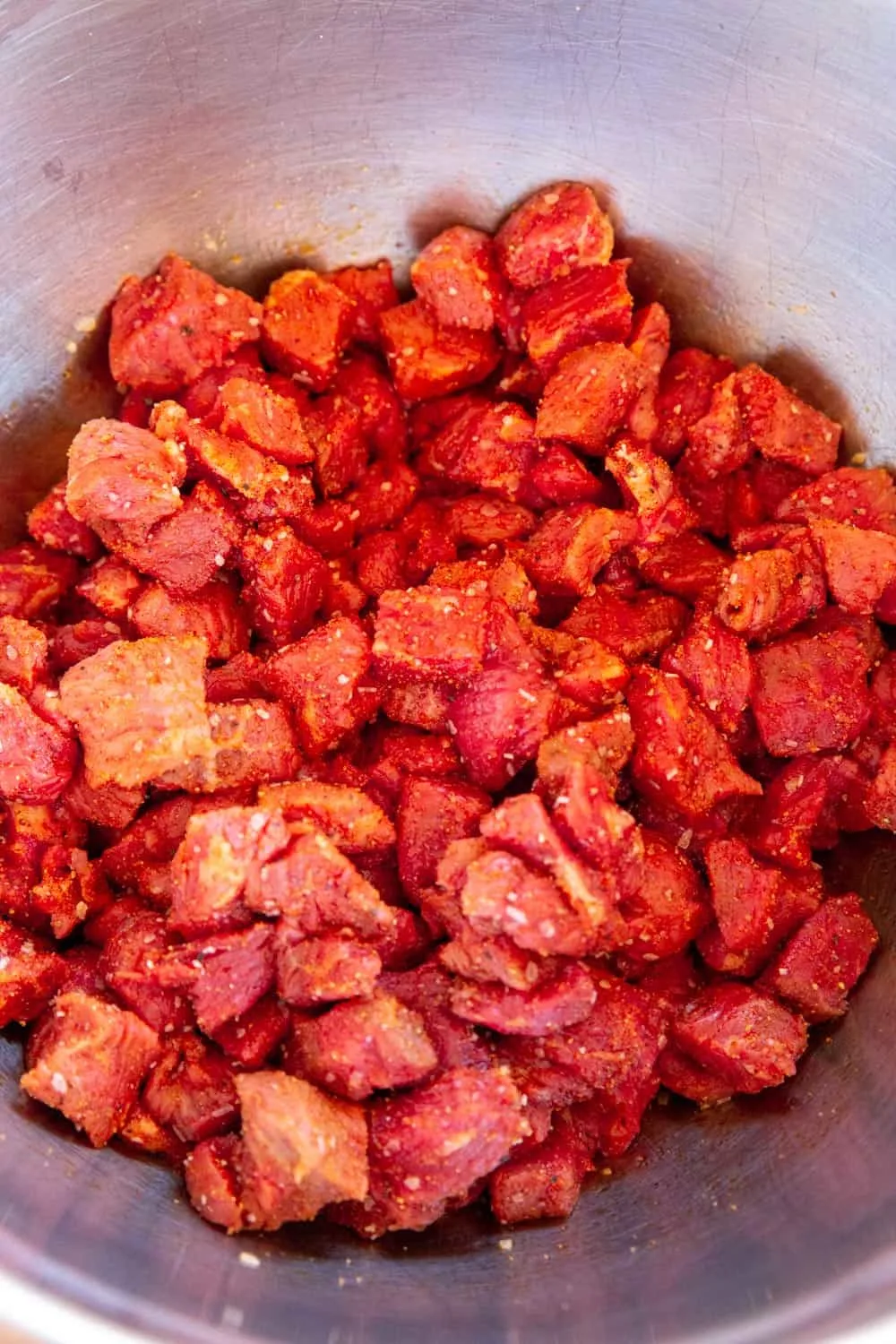 A shiny metal bowl full of small chunks of raw beef, tossed in the carne asada dry rub recipe. 