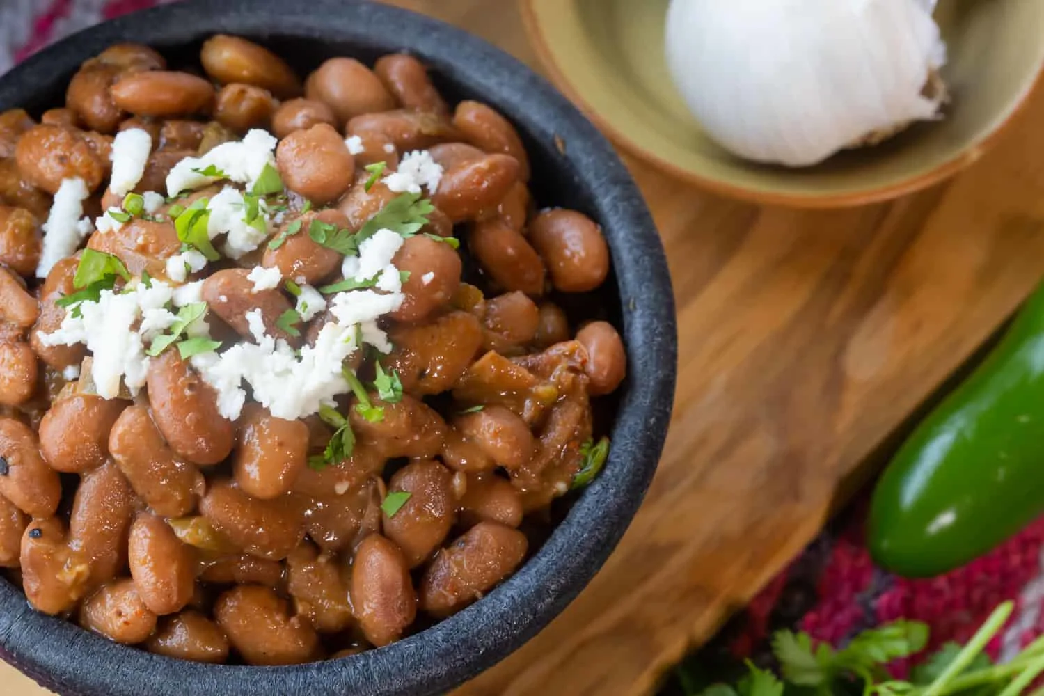 A bowl of glistening cooked pinto beans topped with cilantro and crema.