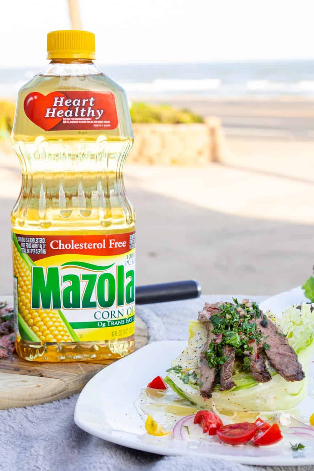 A wedge salad topped with chimichurri skirt steak in front of the ocean