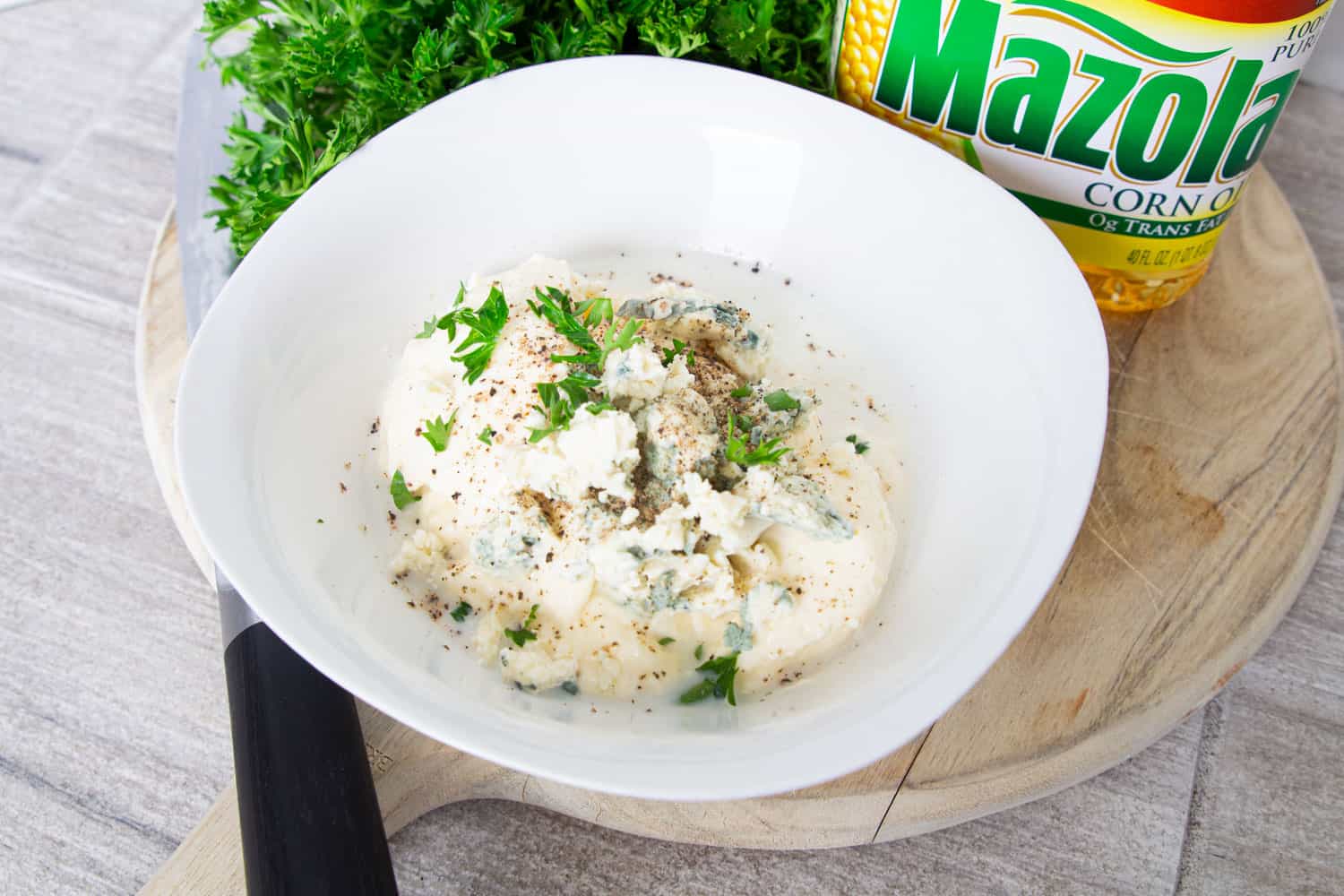 A bowl of homemade blue cheese dressing ingredients: mayonnaise, blue cheese, garlic, milk, and fresh herbs