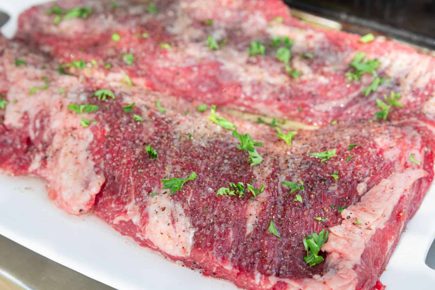 Seasoned skirt steaks (raw) being prepared for the grill