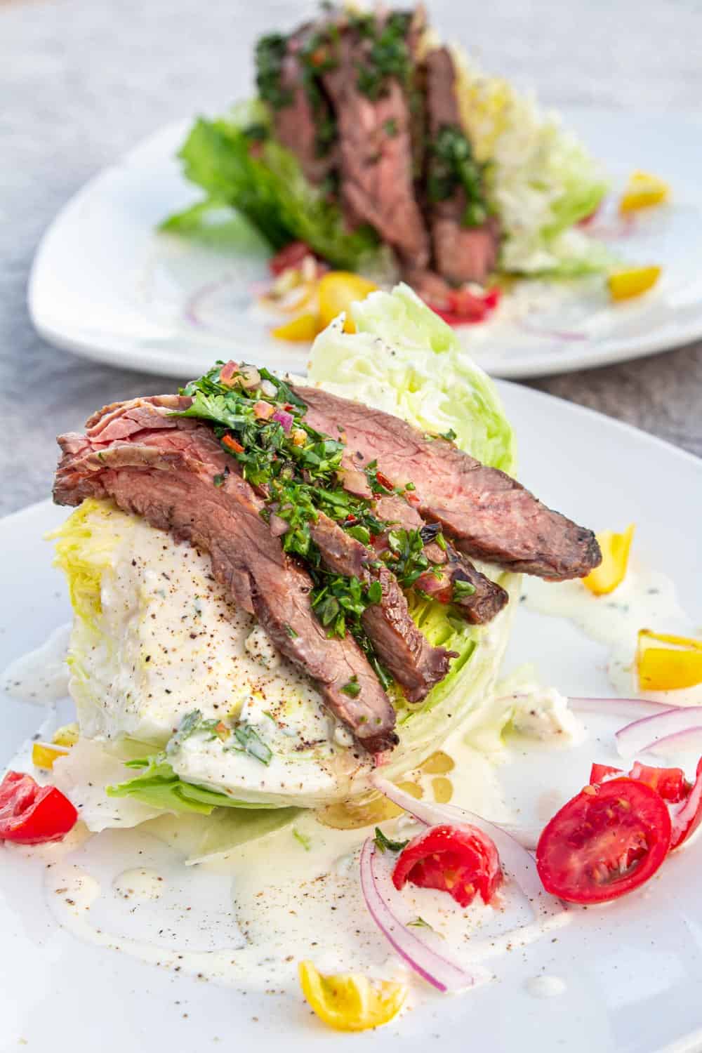 A wedge salad topped with chimichurri skirt steak in front of the ocean