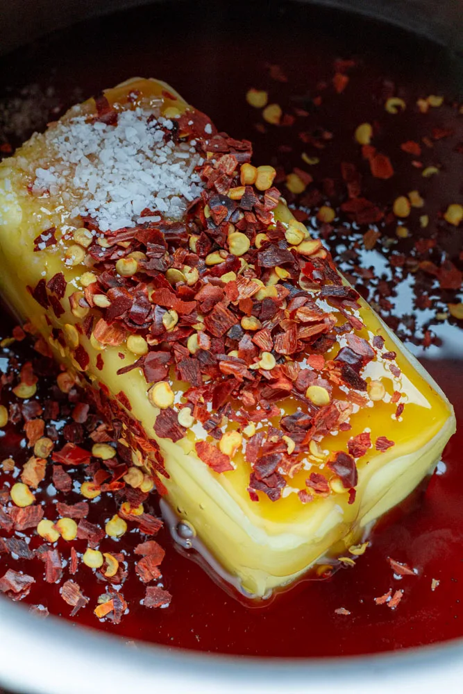 A bright log of butter topped with dry red pepper flakes, kosher salt, and glistening honey