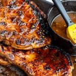 Juicy pork chops next to the grill with a bowl of hot honey butter