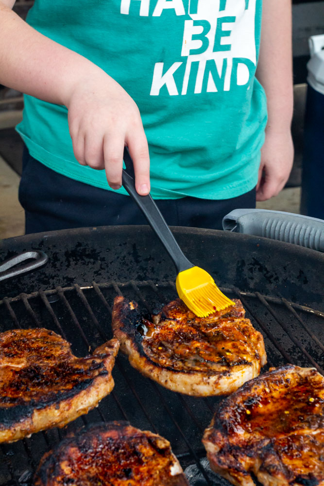 My little boy standing in front of the grill glazing the pork chops with hot honey. 